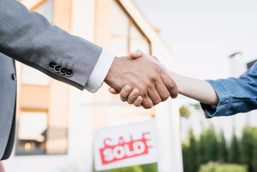 Cropped view of broker nad woman shaking hands with blurred sign with sold lettering